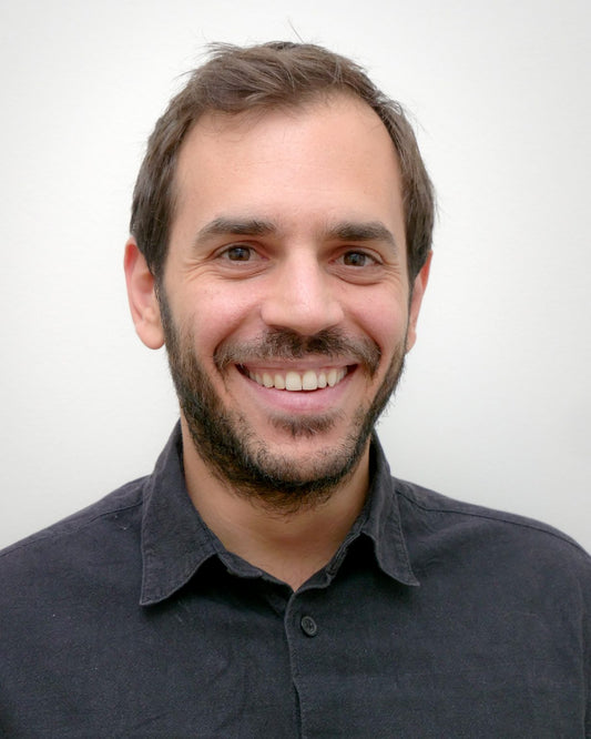 Panagiotis Tsintavis, Integrative Dietitian in Athens, smiling in clinic with fresh vegetables and nutrition books visible in background.
